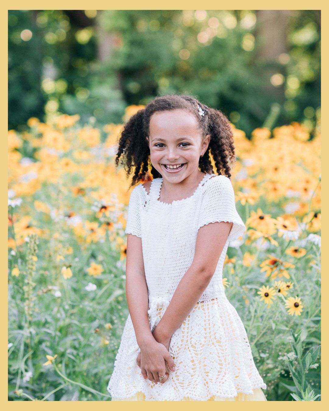 Smiling young girl in white dress standing in a field of yellow black-eyed Susan flowers outdoors.