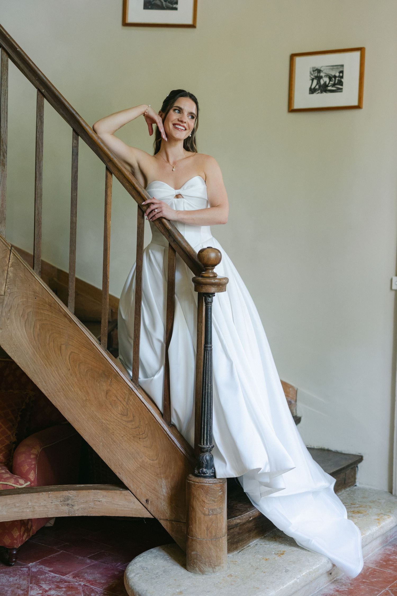 Smiling bride in strapless white gown posing on wooden staircase in elegant venue.
