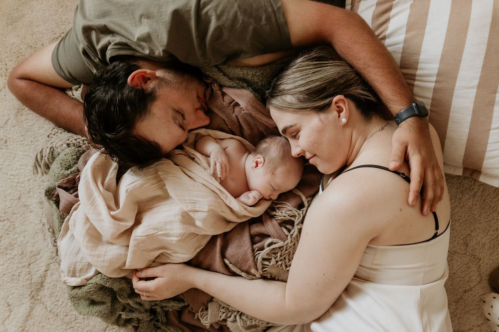 New parents lying down with their newborn baby between them indoors.