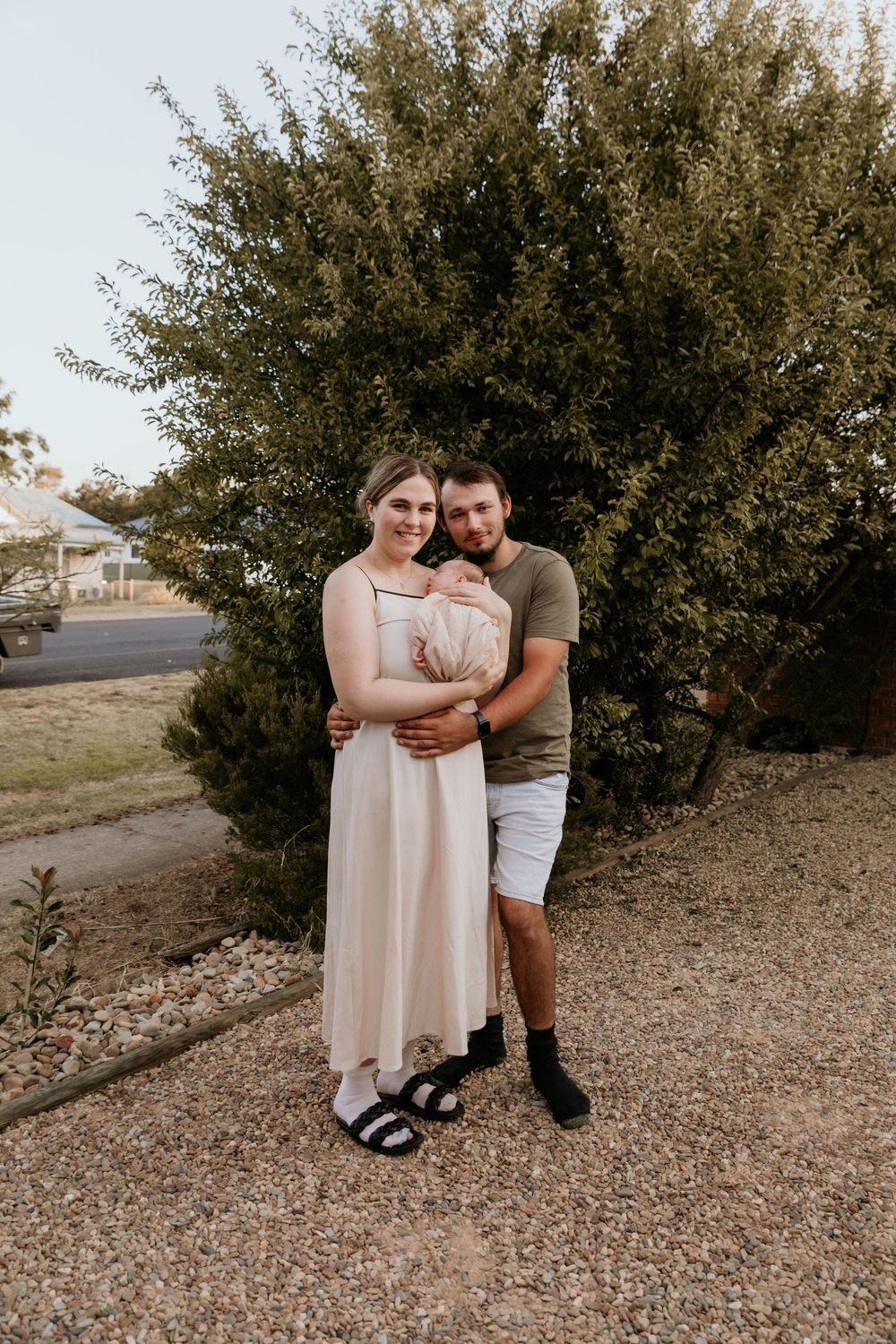 Young couple standing together outdoors holding their newborn baby.