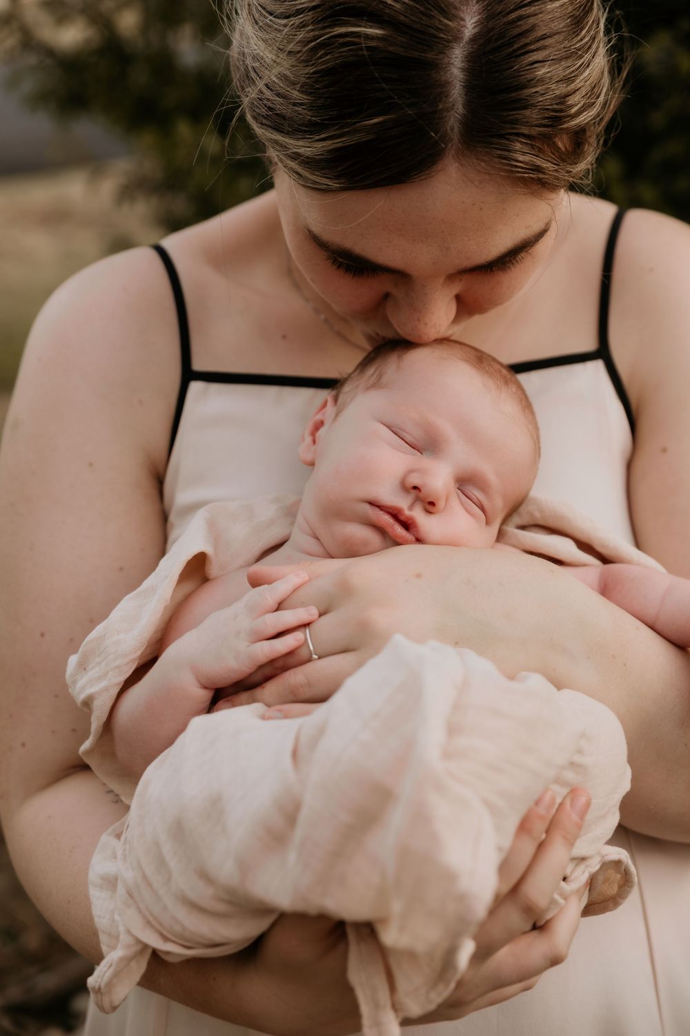 Mother gently kissing her sleeping newborn baby while holding them close.