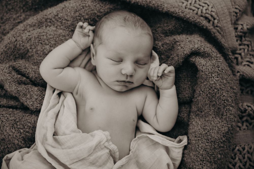 A peaceful black and white close-up of a sleeping newborn baby lying on soft textured blankets.