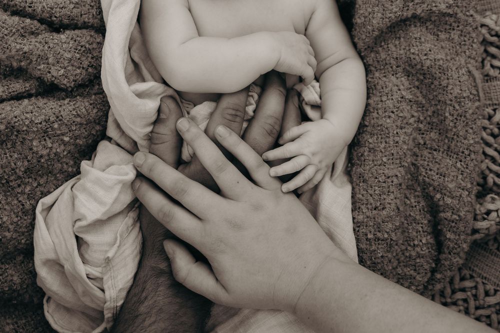 A black and white close-up of parents gently cradling their newborn babys tiny hands and feet.