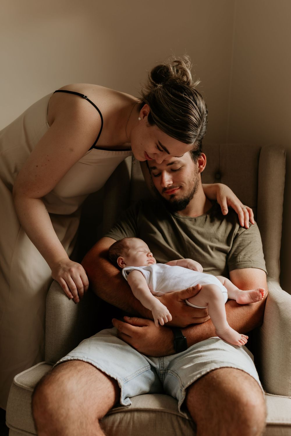 Loving parents bonding together over their sleeping newborn baby in a nursery chair.