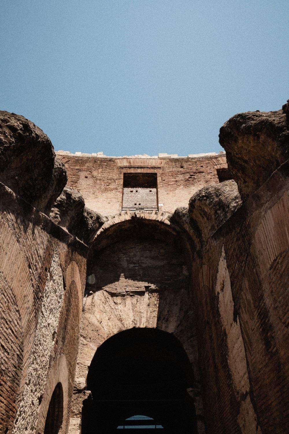 Ancient Roman ruins with a large stone arch and weathered brick walls against a clear blue sky.