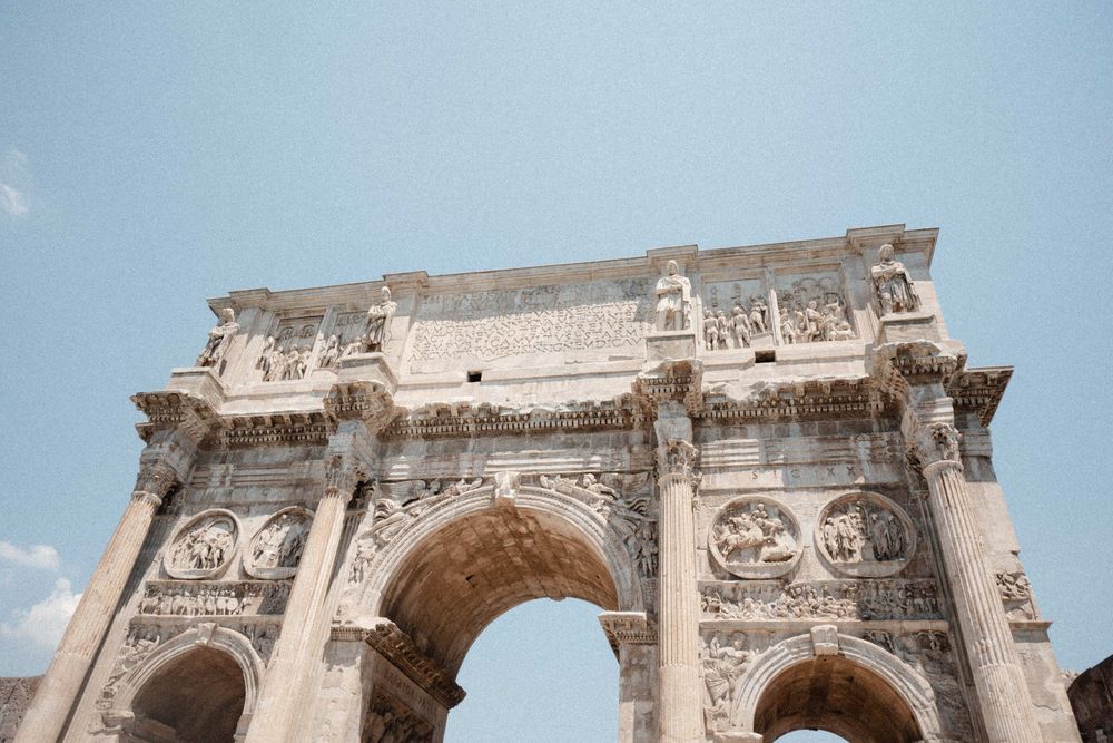 Ancient Roman triumphal arch with intricate stone carvings and reliefs against a clear blue sky in Rome, Italy.