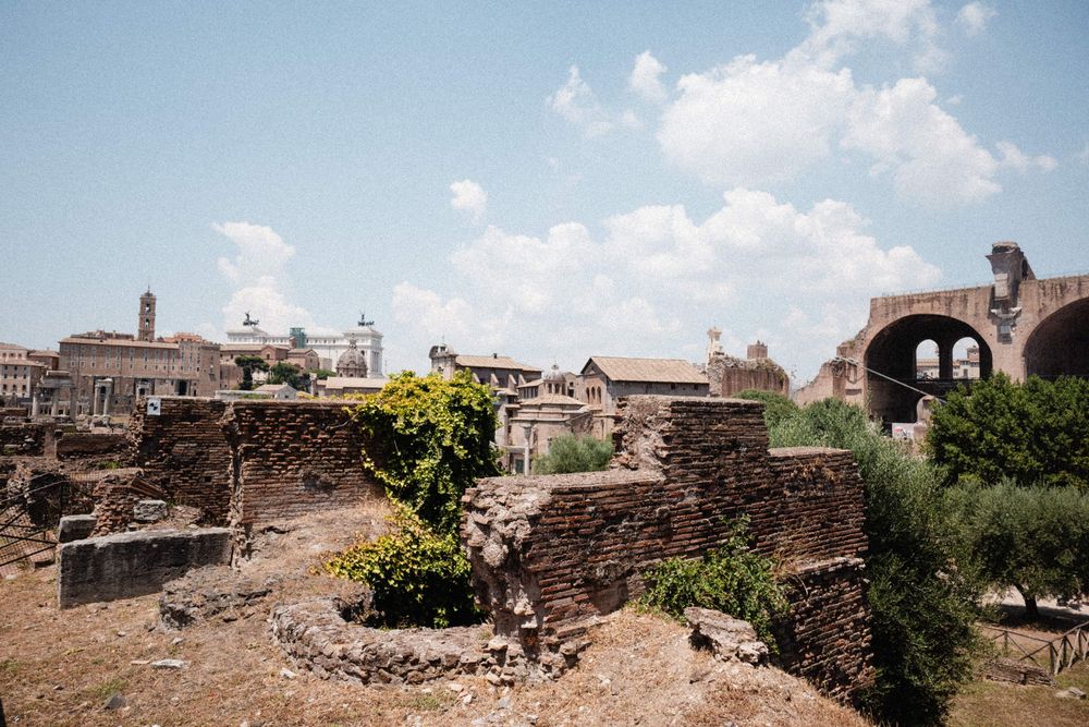 Ancient Roman ruins with stone walls, arches, and lush greenery under a bright blue sky in Rome, Italy.