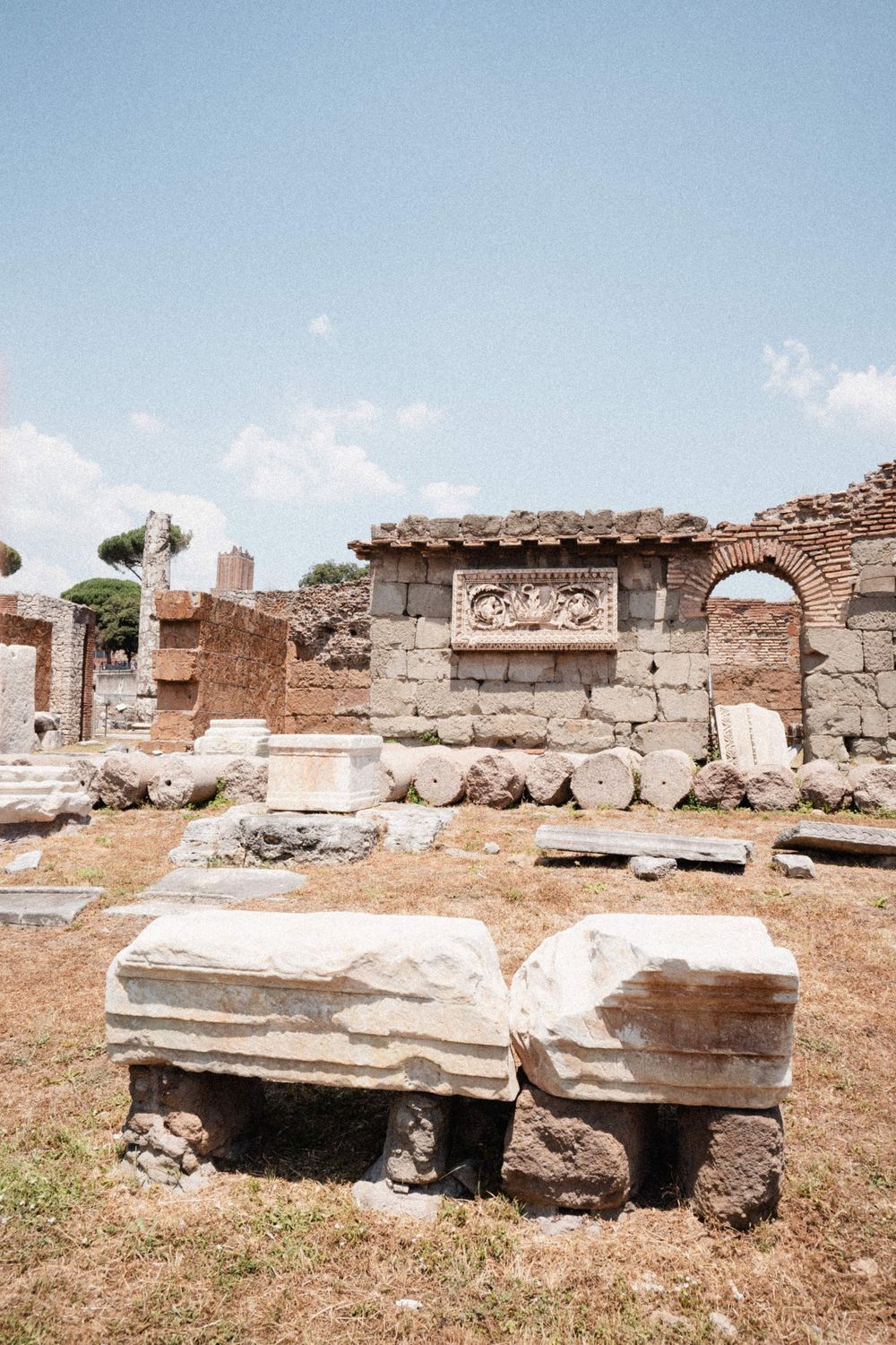 Ancient Roman ruins with marble fragments and decorative relief wall under a bright blue sky.