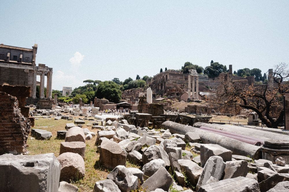 Ancient Roman Forum ruins with scattered marble columns and stone debris under a bright summer sky in Rome, Italy.