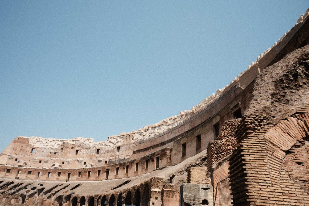 Interior view of the ancient Roman Colosseum showing weathered brick arches and tiers against a clear blue sky.