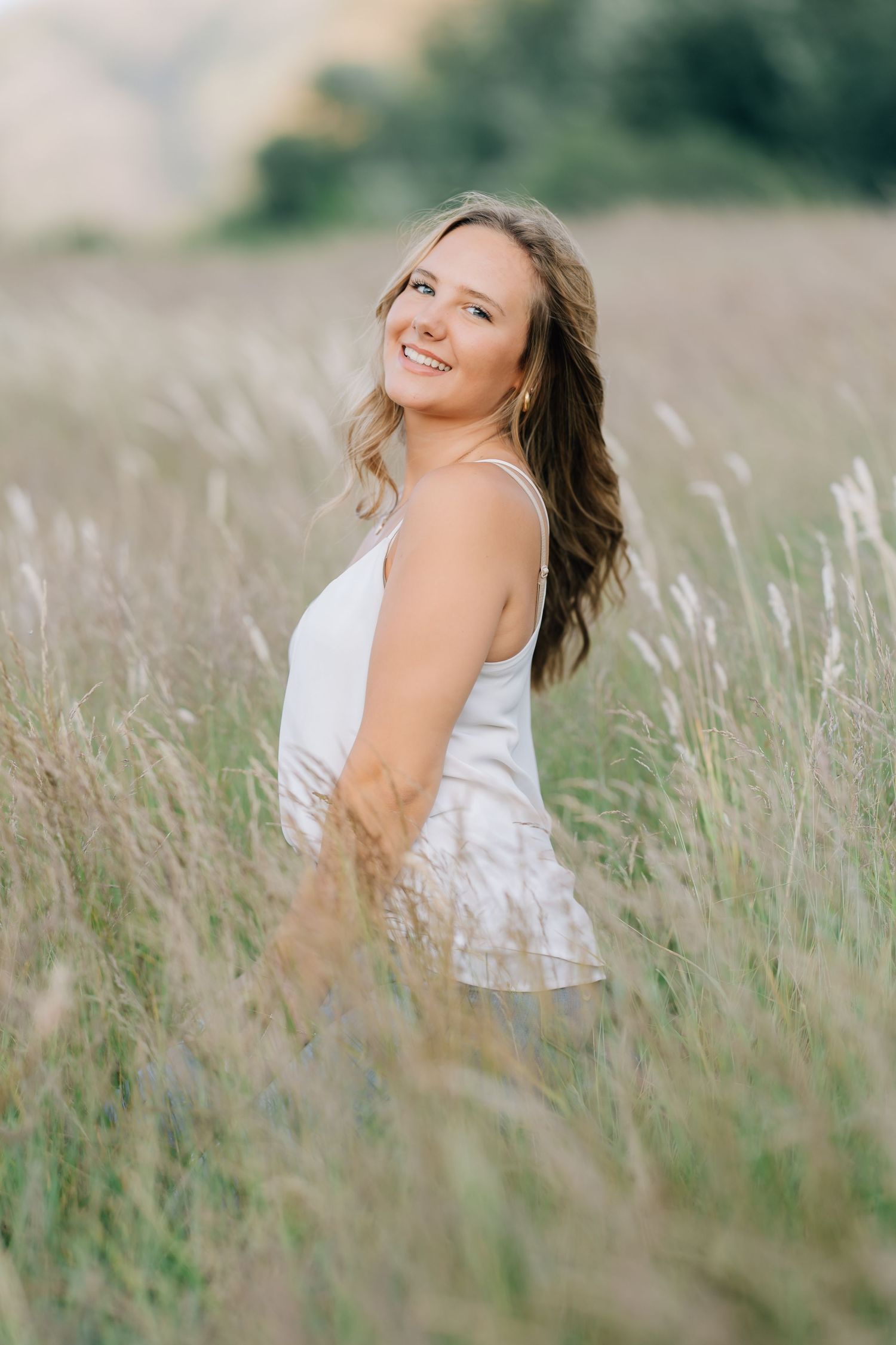 Young woman in white dress smiling in a golden field of tall grass during golden hour.