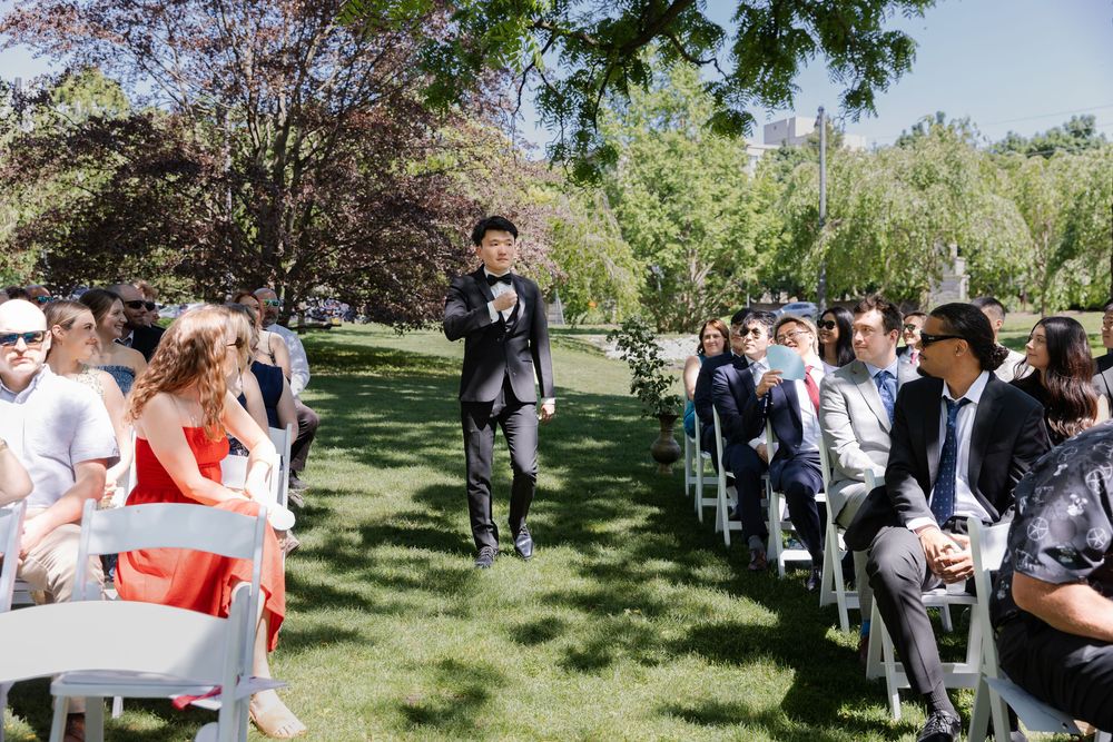 Groom walks down the aisle surrounded by guests during outdoor ceremony at the civic garden complex in london, ontario.