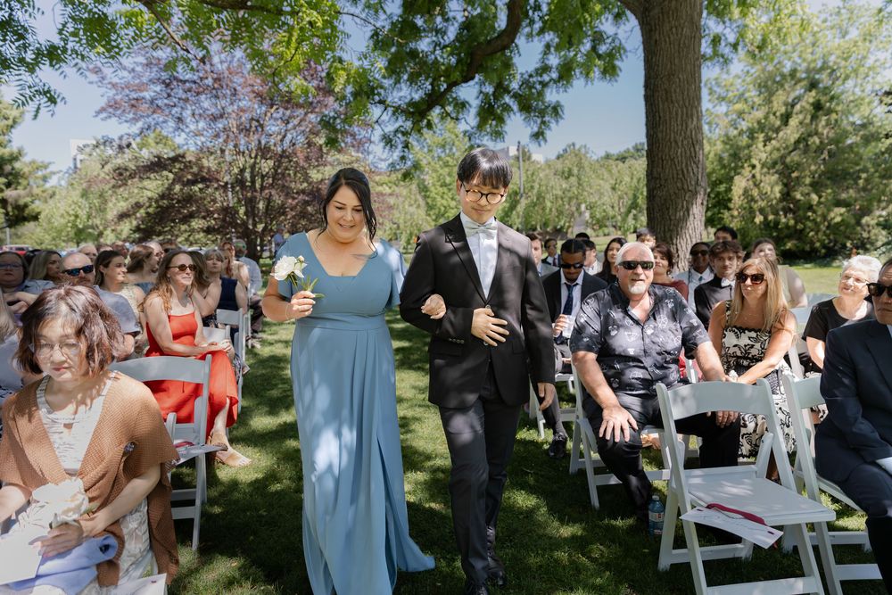Bridesmaid and groomsmen walking down aisle surrounded by guests at an outdoor ceremony at the civic garden complex in london, ontario.