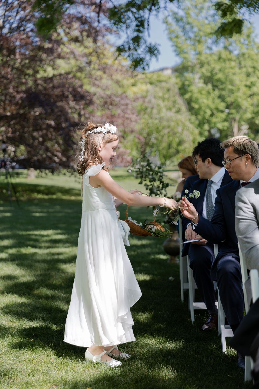 Flower girl hands out flowers down the aisle of an outdoor wedding ceremony under the trees at the civic garden complex in london, ontario.