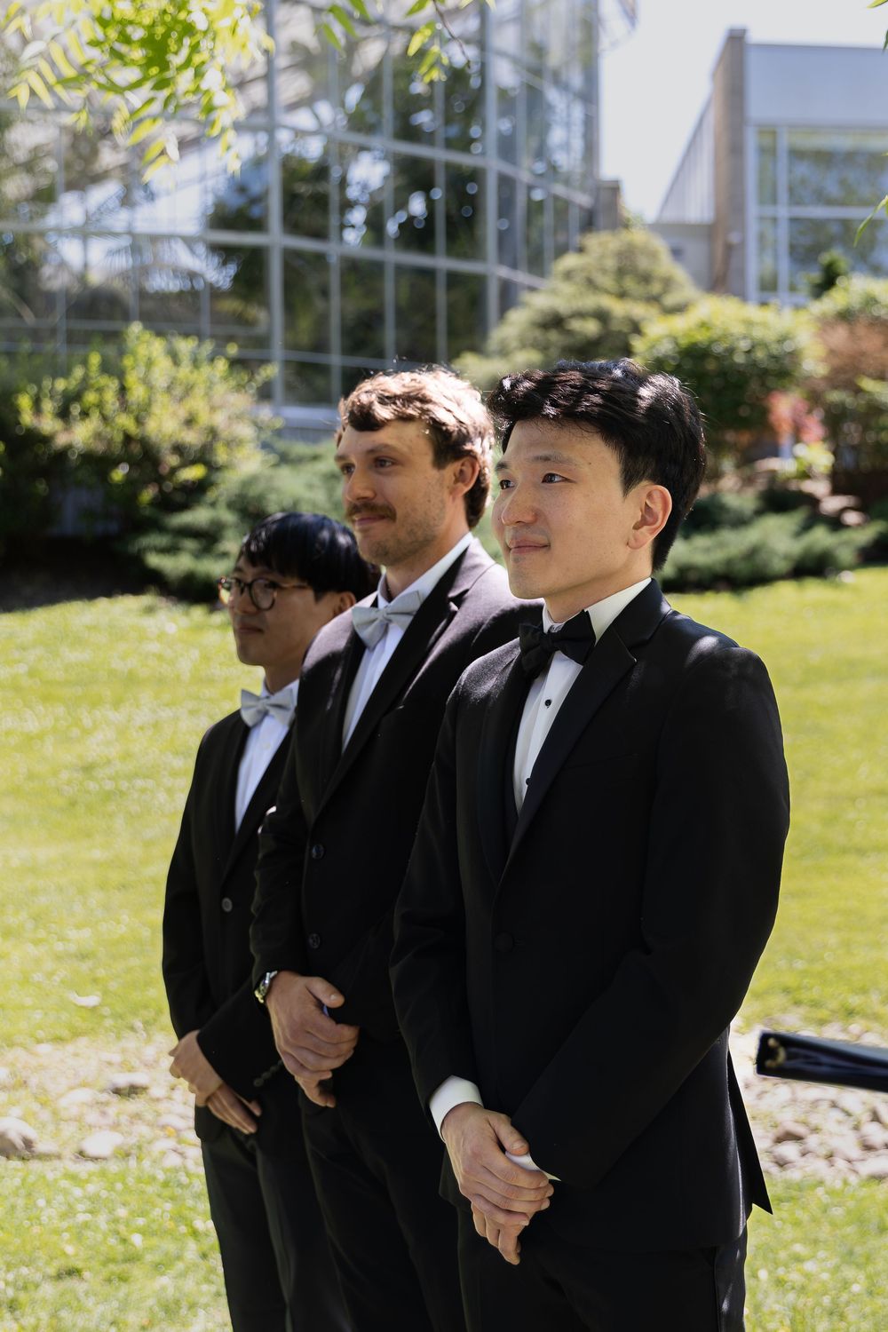 Groom stands with groomsmen at their outdoor ceremony under the trees at the civic garden complex in london, ontario.