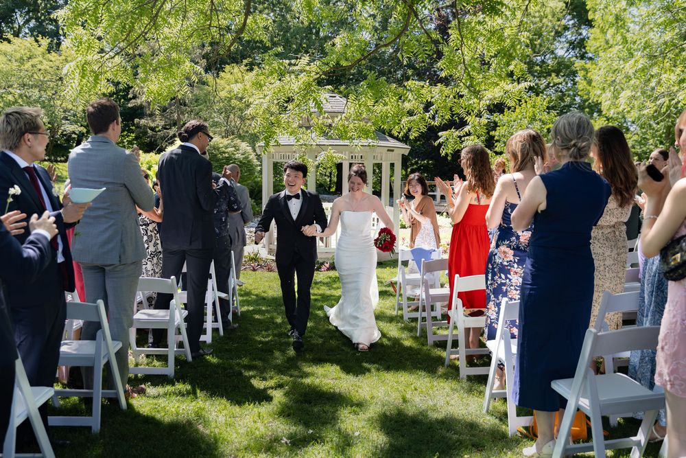 Bride and groom celebrate with their guests during their ceremony under the trees at the civic garden complex in london, ontario.