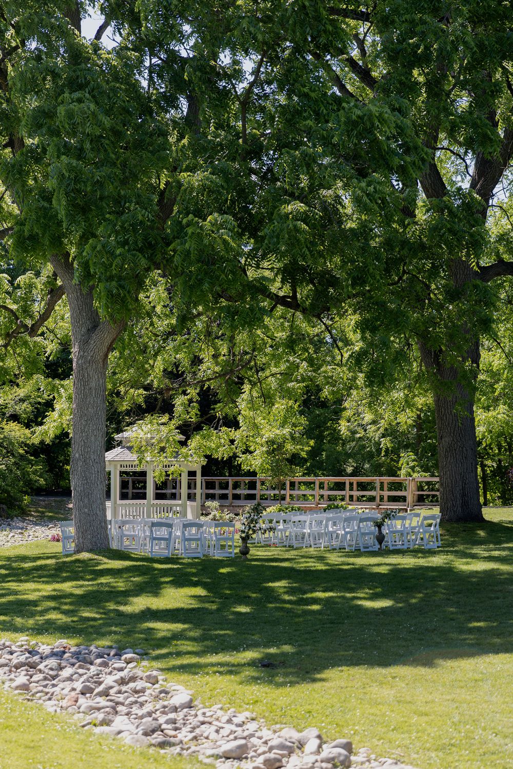 Wedding ceremony with white chairs under large trees beside a gazebo on a lush green lawn at civic garden complex in london ontario.