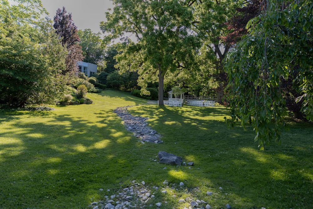Lush green garden with stone path, large trees, manicured lawn, and white gazebo at civic garden complex in london ontario.