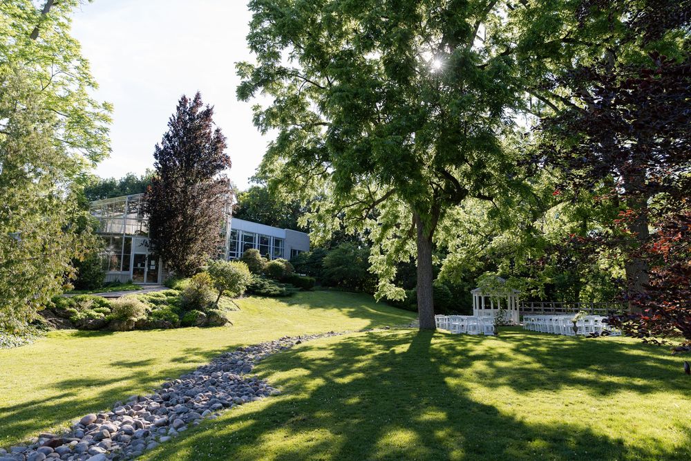 Lush green lawn and a modern building with large windows, framed by tall trees in a garden setting at civic garden complex in london ontario