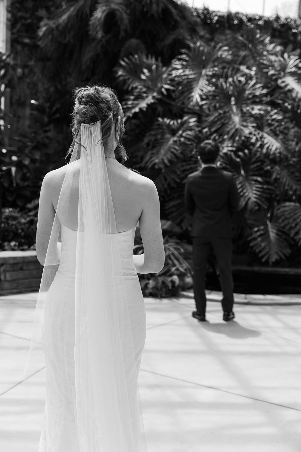 Black and white photo of bride walking towards groom in the conservatory at the civic garden complex in london, ontario.