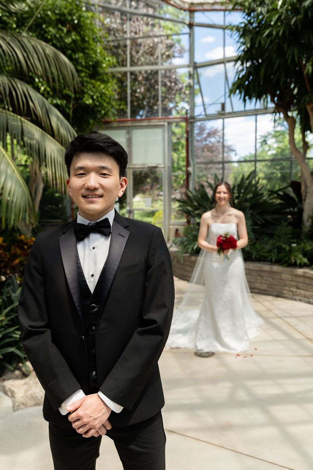 Groom standing with bride in the background during first look in the conservatory at the civic garden complex in london, ontario.