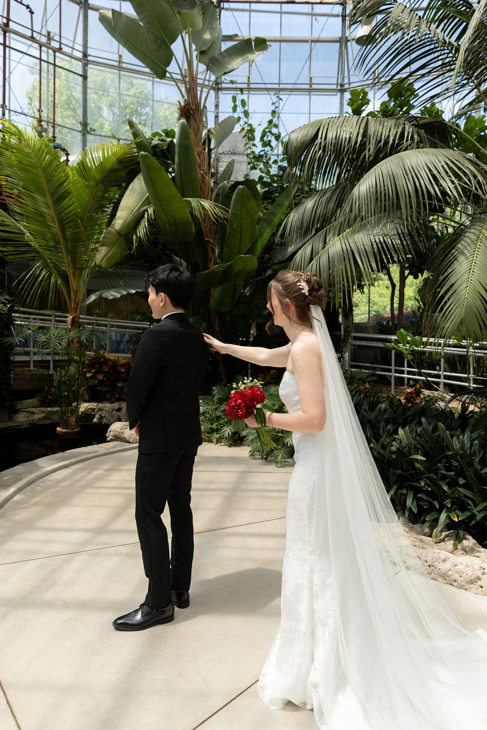 Bride touching groom on the shoulder during first look at the conservatory at the civic garden complex in london, ontario.