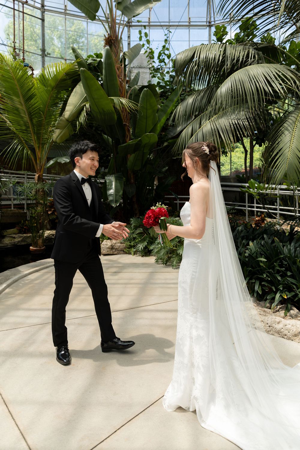 Groom smiling at bride surrounded by greenery in the conservatory during first look at the civic garden complex in london, ontario.