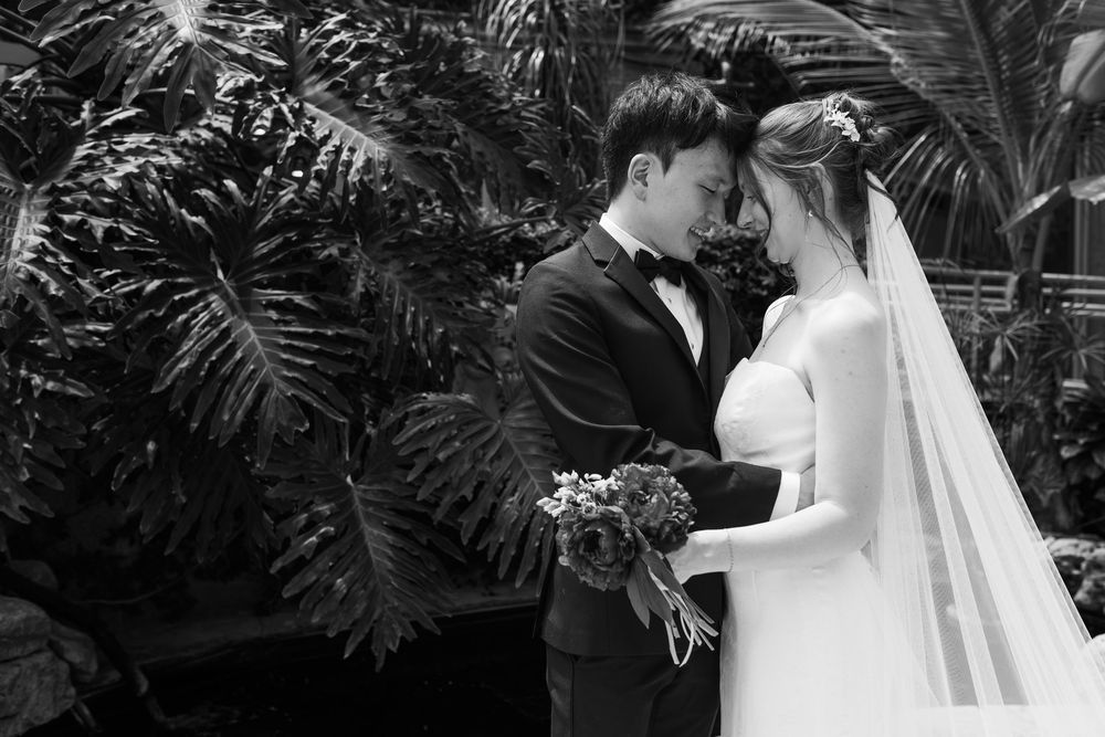 Black and white photo of bride and groom resting their heads together in the conservatory at the civic garden complex in london, ontario.