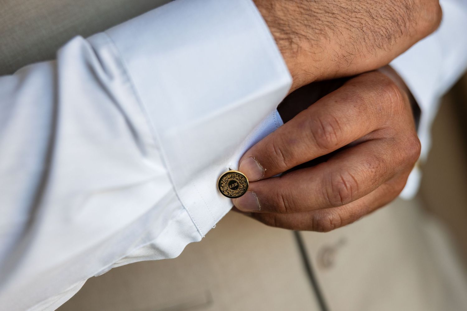 Close-up of a groom fastening a decorative gold cufflink on his white dress shirt sleeve.