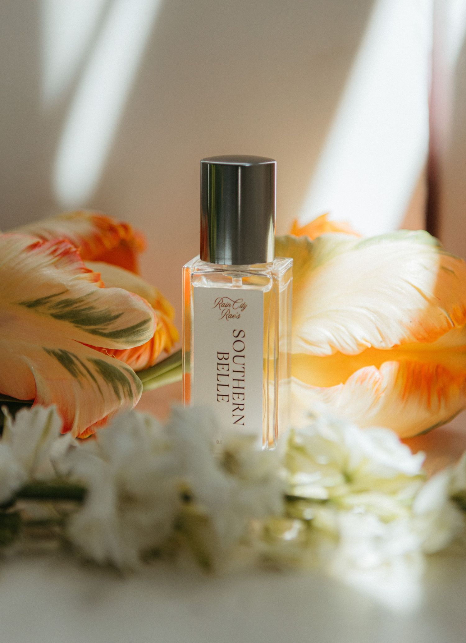 Southern Belle perfume bottle surrounded by orange and white flowers on a soft light background.