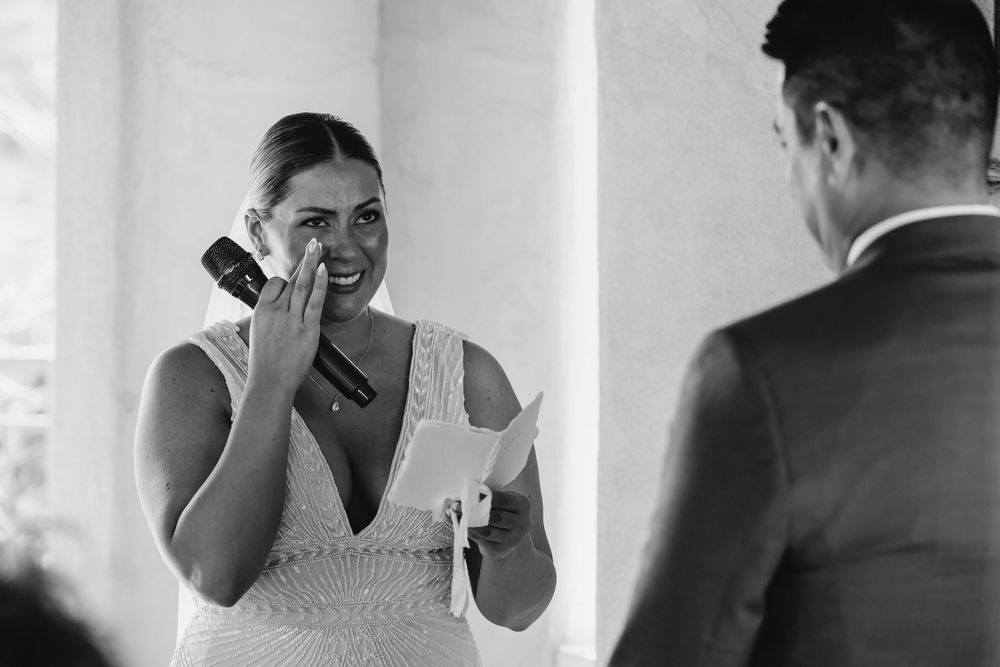 Emotional bride wiping tears while reading wedding vows at ceremony.