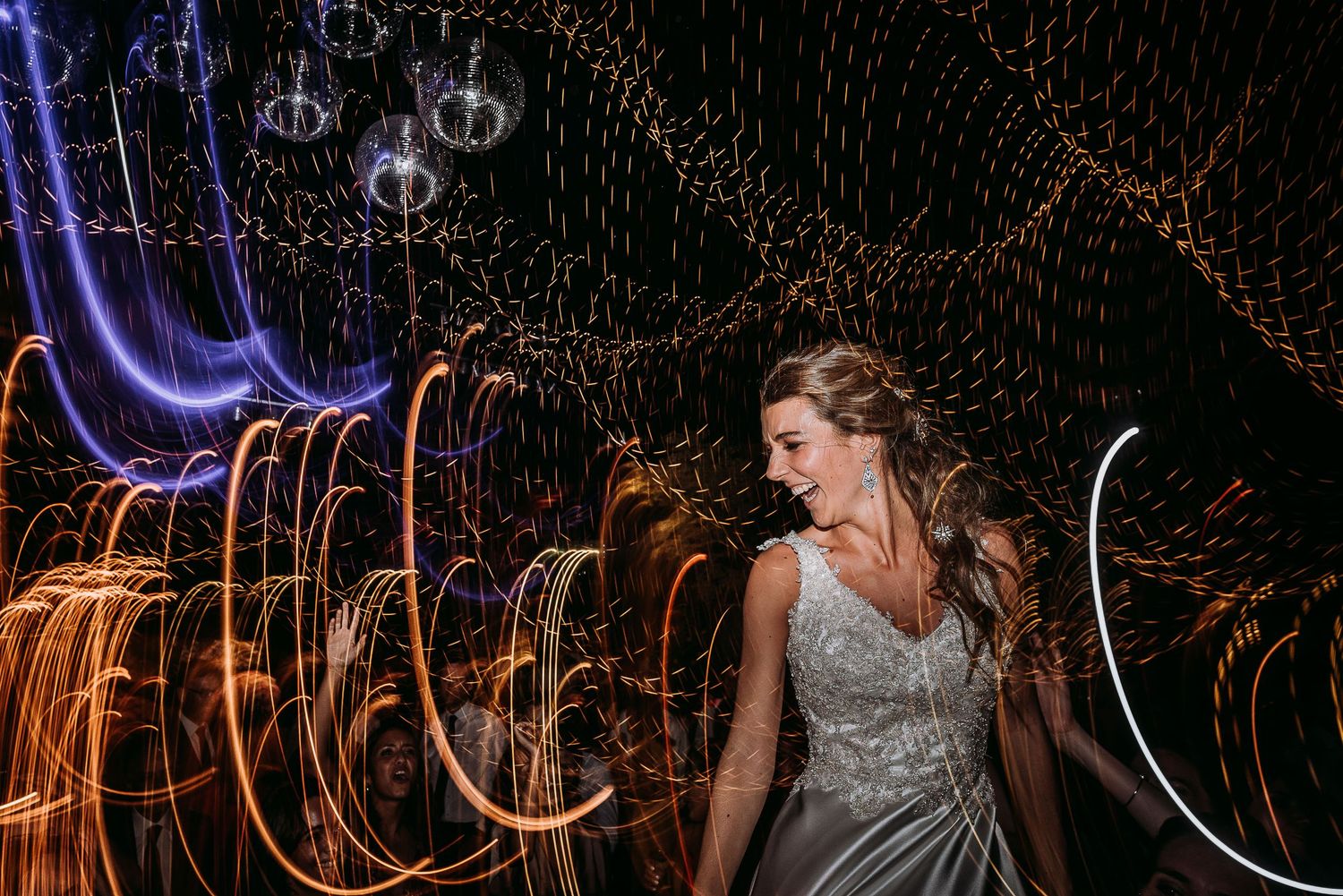 Bride dancing with swirling light trails creating a magical bokeh effect at a wedding reception.