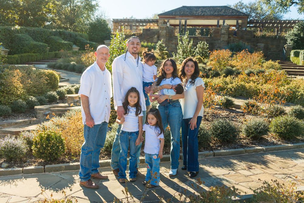 Family of seven posing together in a scenic garden park with lush greenery and a pergola in the background.