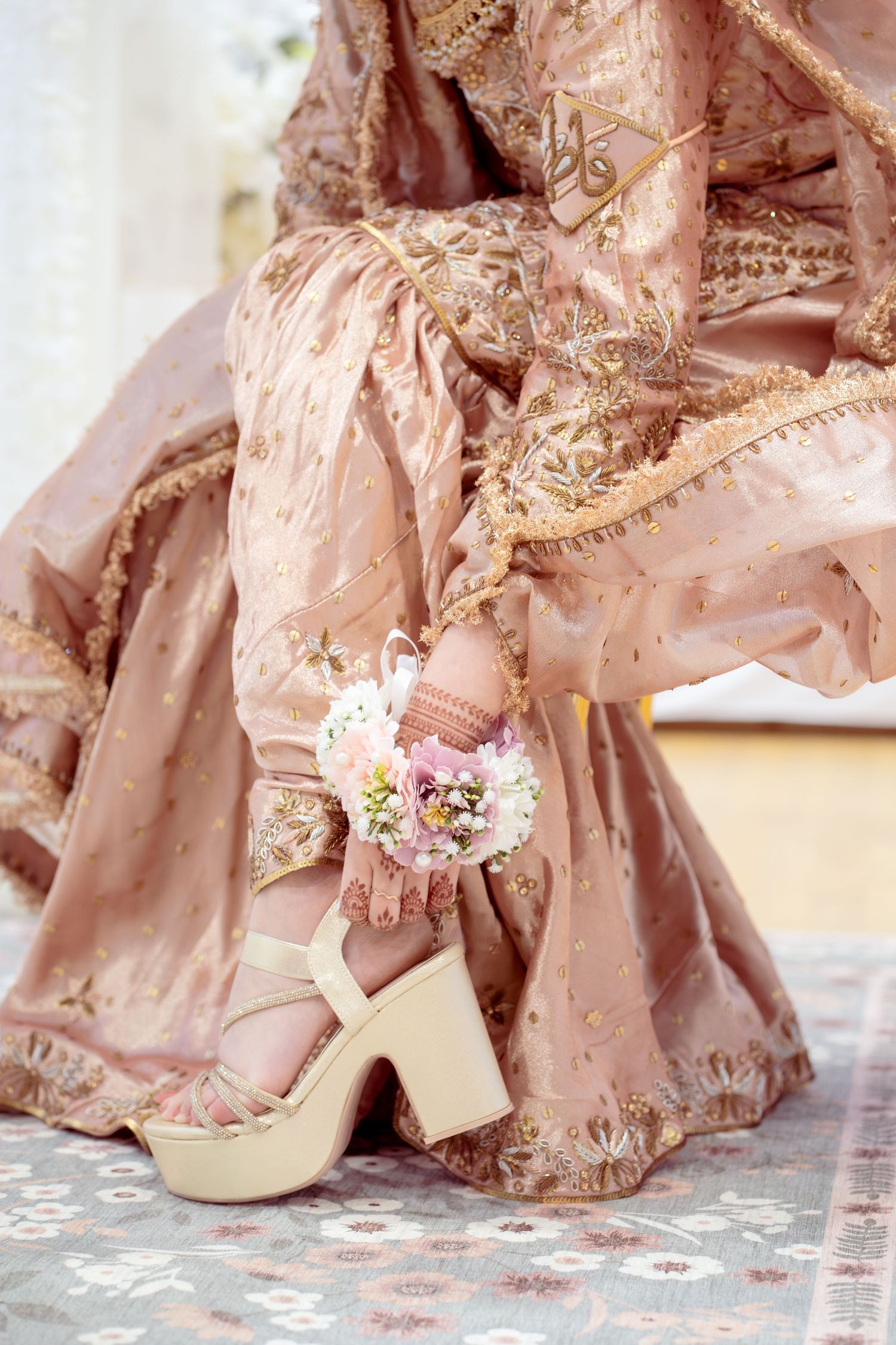 Bride in dusty rose embroidered lehenga with floral ankle bracelet and cream block heel sandals.