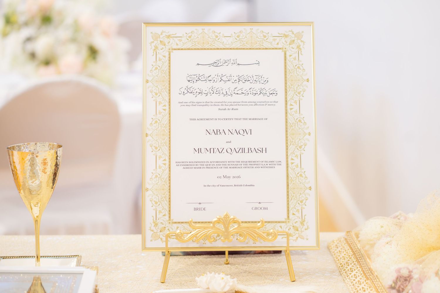 Elegant gold and white Islamic wedding Nikkah certificate displayed on decorative easel with floral decor.
