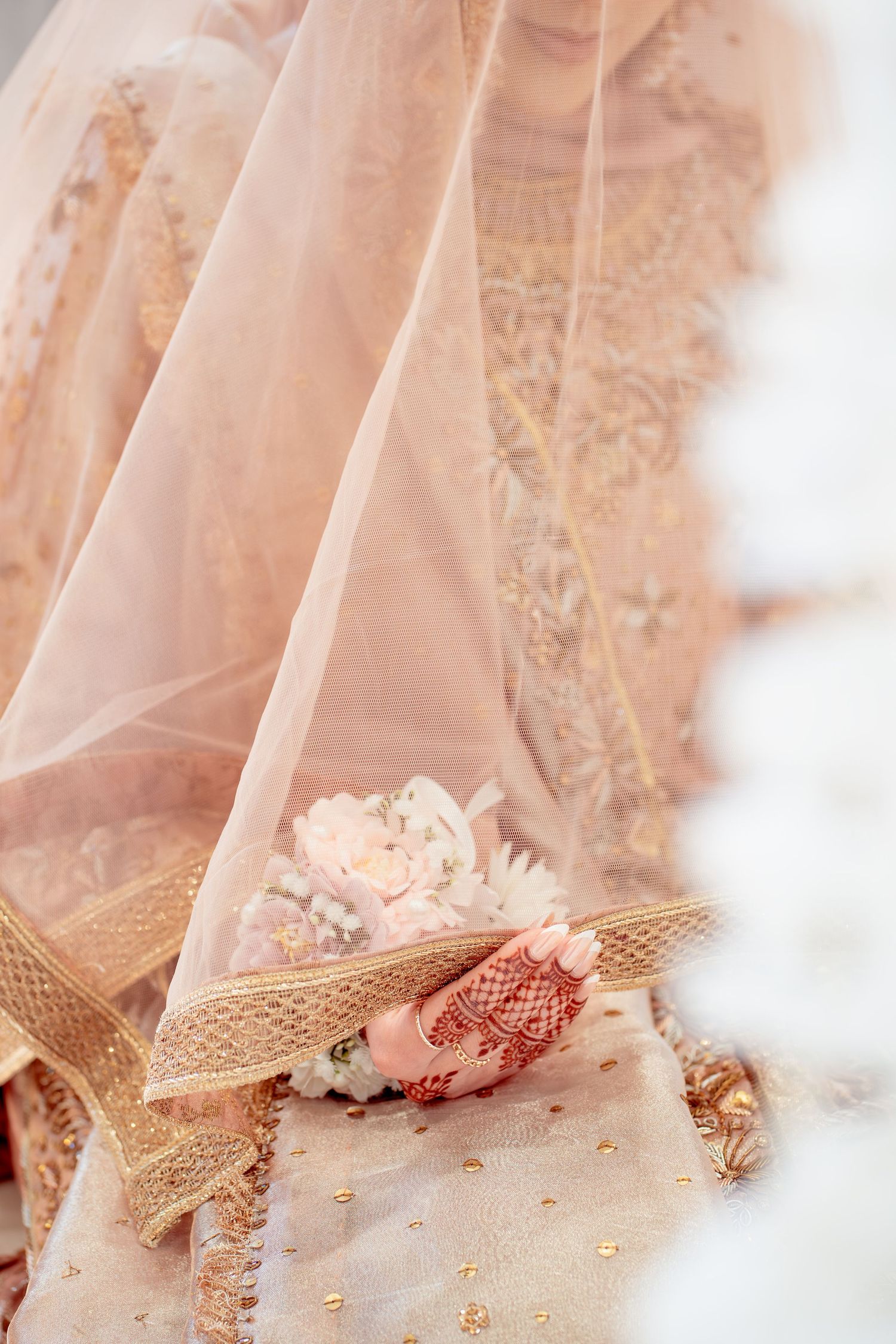 Bride in ornate blush pink Indian bridal lehenga with gold embroidery holding a delicate floral bouquet.