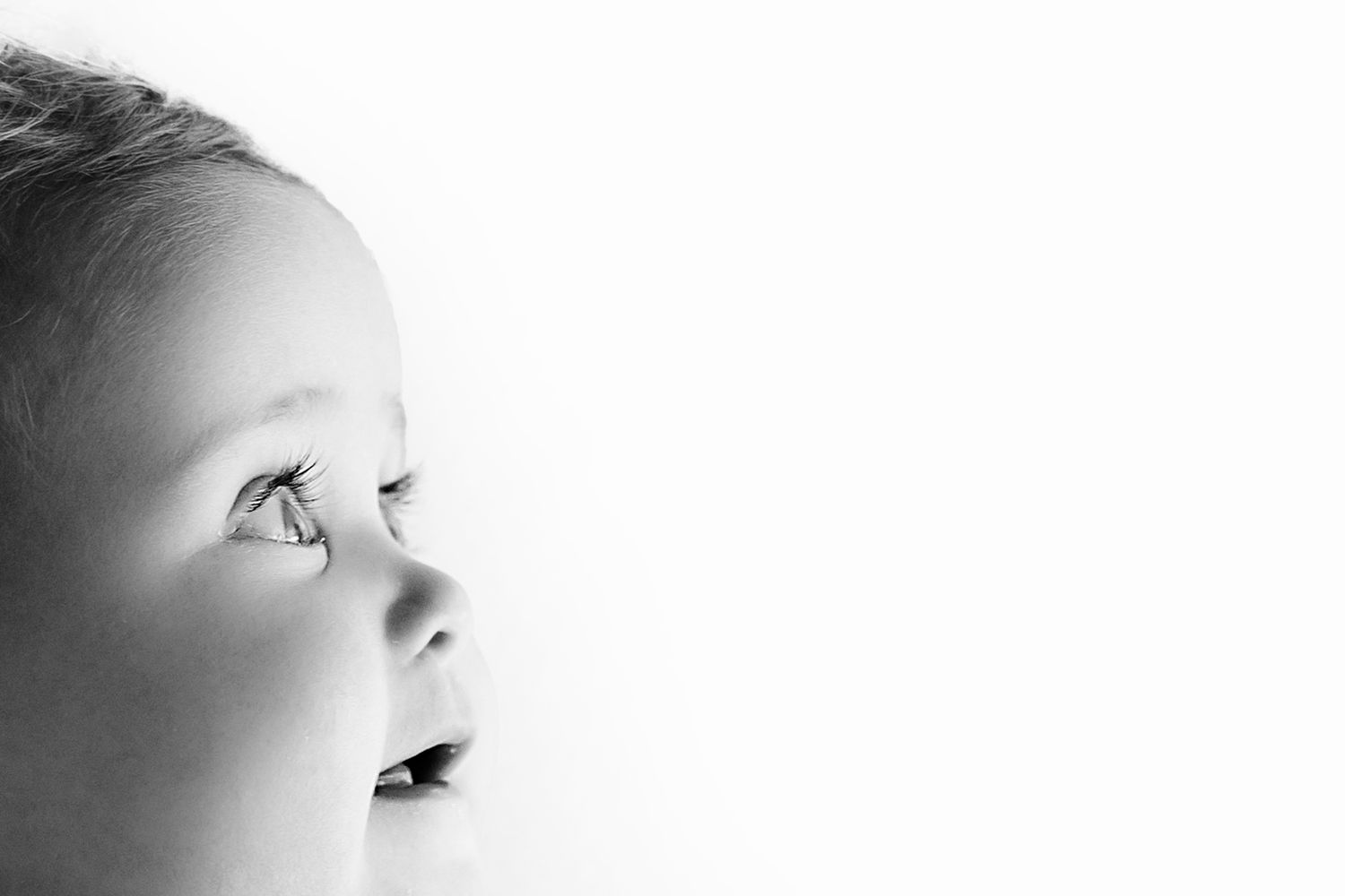 Black and white close-up portrait of a young baby looking upward with soft lighting.