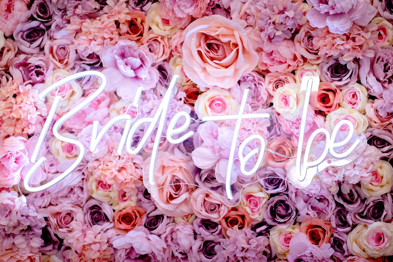 Neon pink Bride to Be sign glowing against a lush wall of pink and blush roses for a bridal shower.