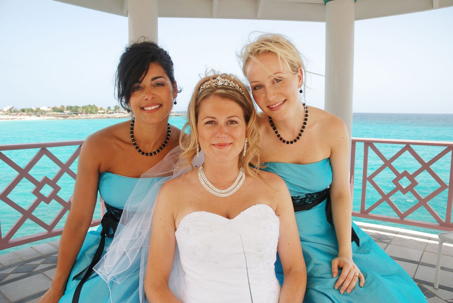 Bride in white gown with two bridesmaids in teal dresses posing in a gazebo by the ocean.