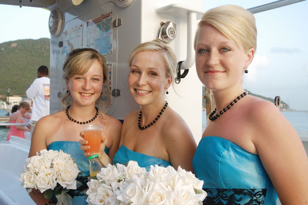 Three bridesmaids in matching turquoise dresses holding white floral bouquets at outdoor wedding reception.
