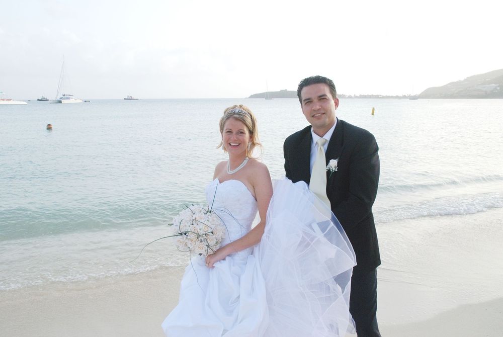 Smiling newlywed couple in wedding attire poses romantically on tropical sandy beach by calm ocean.