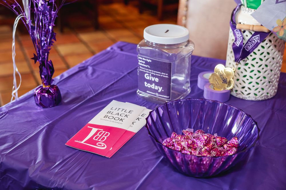 Purple table display with Give Today donation jar, Little Black Book, candy bowl, and decorative items for a charity event.