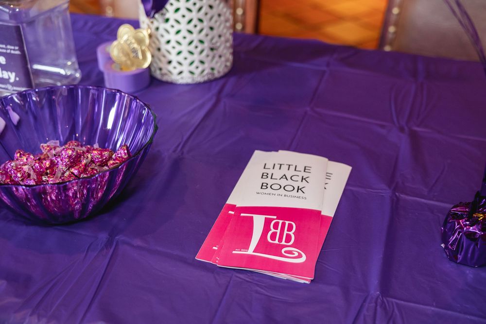 Little Black Book pamphlet on purple tablecloth beside purple glass bowl filled with pink candies.