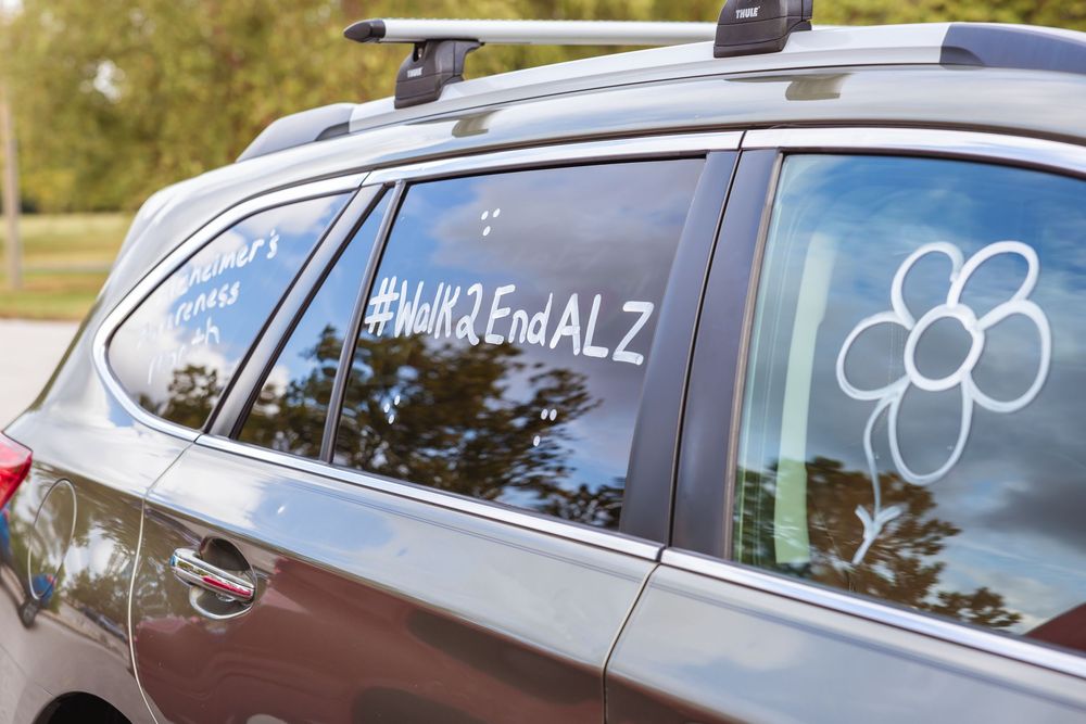 Car window with #Walk2EndALZ decal and flower logo supporting Alzheimer's awareness walk.
