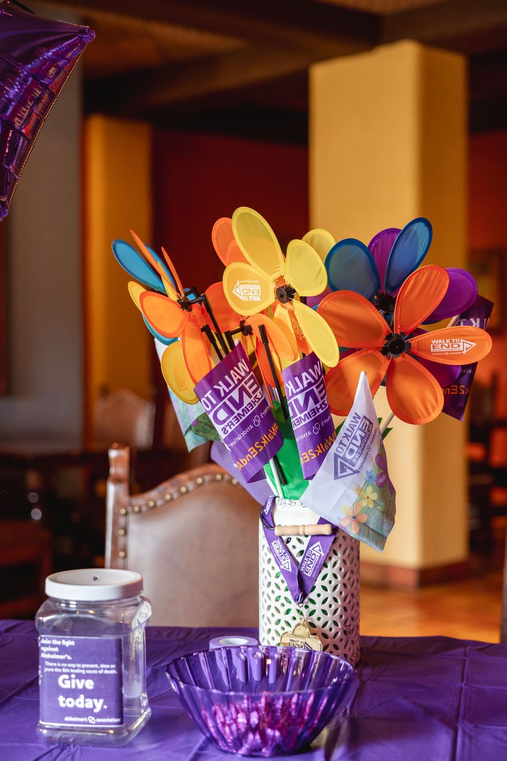 Colorful pinwheel flower arrangement in decorative vase on purple table with donation jar for Alzheimers awareness event.