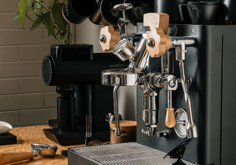 Close-up of a professional black espresso machine with chrome fittings and wooden accents on a kitchen counter.