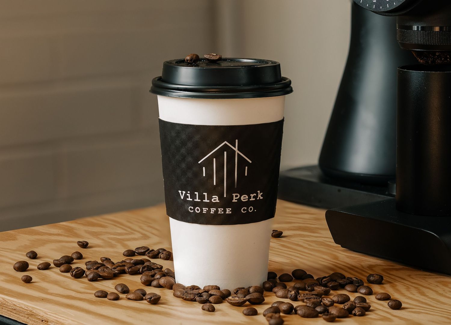 Villa Perk Coffee Co. branded paper cup surrounded by coffee beans on a wooden surface.