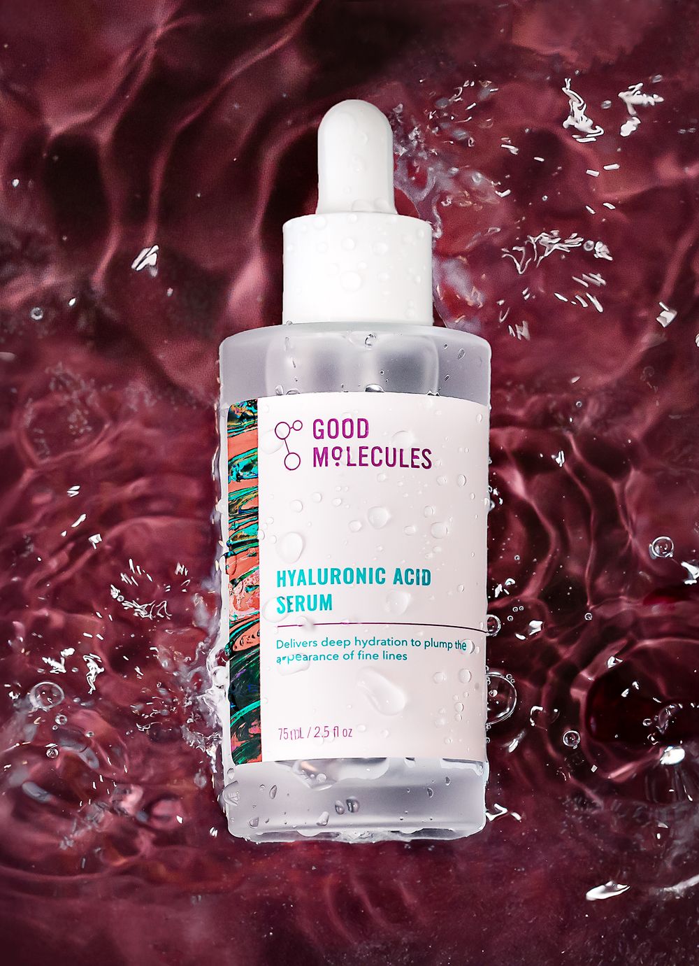 Good Molecules Hyaluronic Acid Serum bottle with dropper, surrounded by water splashes on a deep red background.