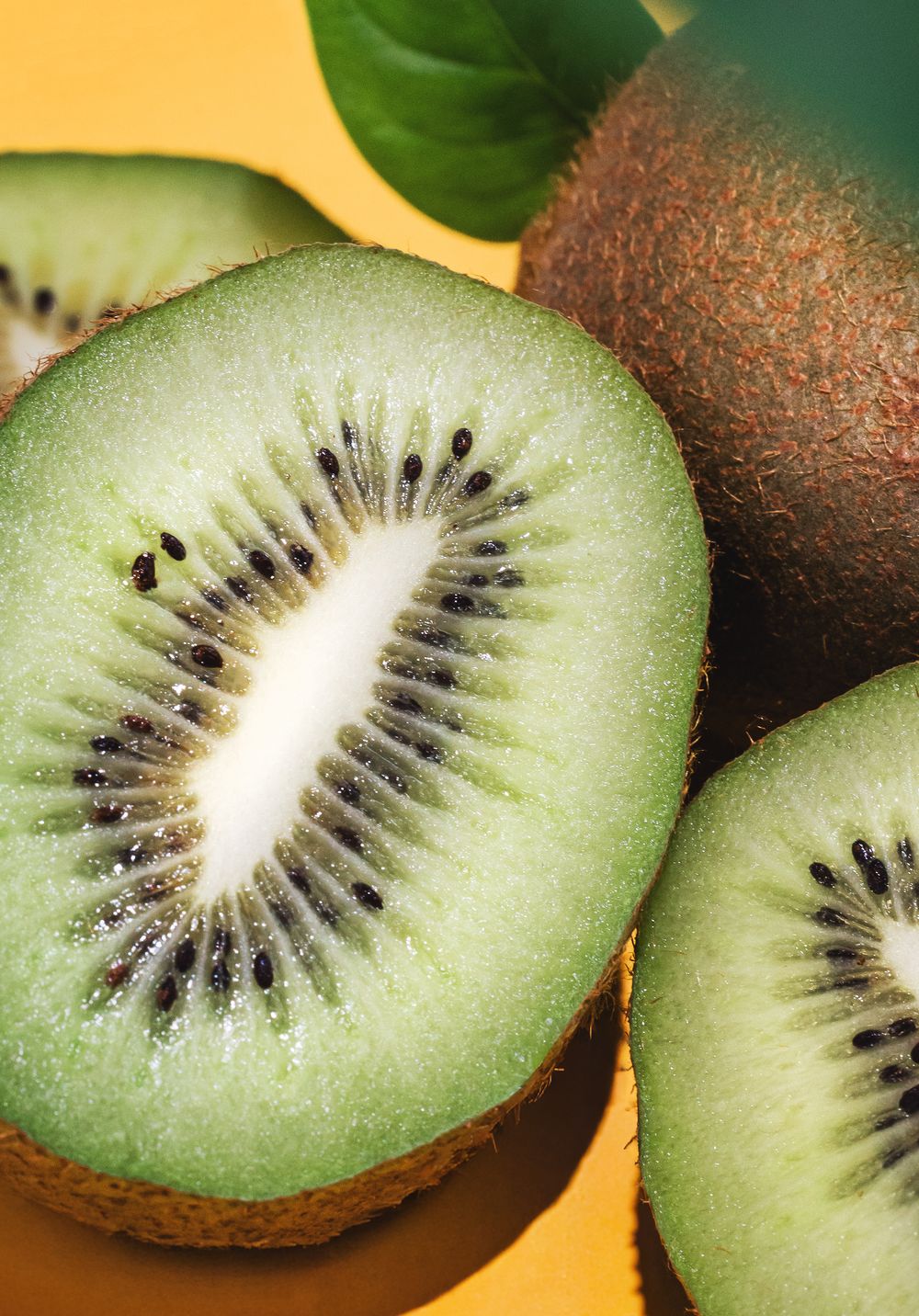 Fresh kiwi fruit sliced in half revealing vibrant green flesh with black seeds, displayed on a yellow background.