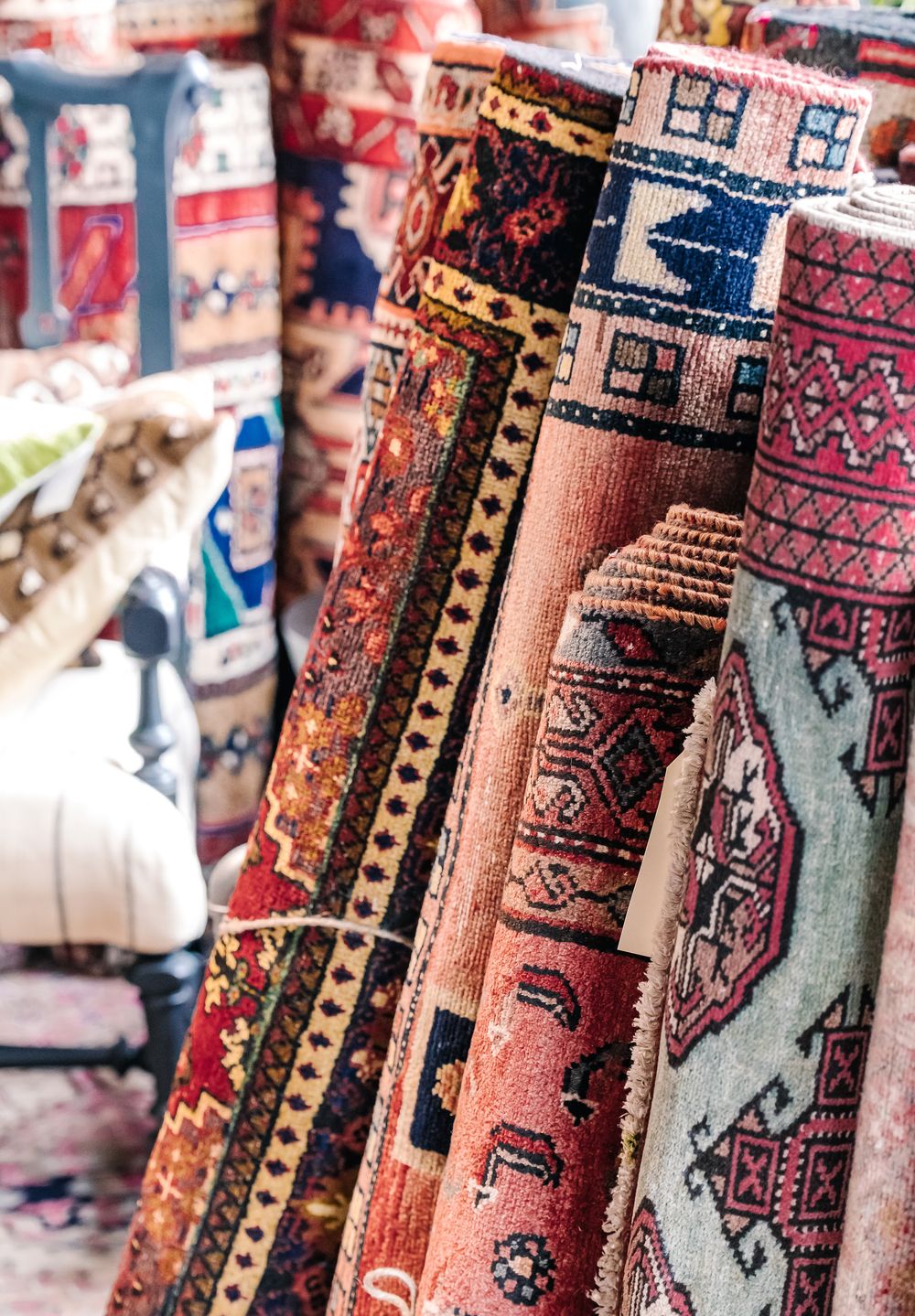 Colorful rolled Persian rugs displayed upright in a market, showcasing intricate geometric patterns in red, blue, and gold.